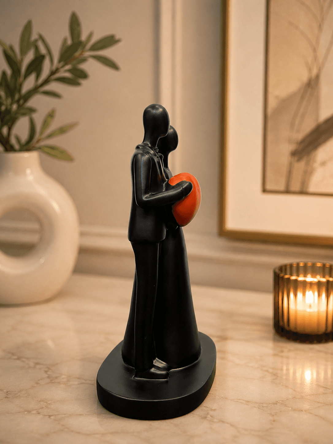 Modern black abstract sculpture of a couple holding a bright red heart, placed on a marble table with candles for romantic bedroom decor preview 2